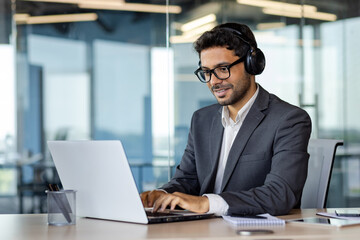 Successful indian programmer working inside office with laptop, man in headphones and business...