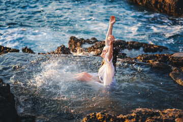 Young cheerful relaxed woman in a white shirt in a natural sea bath on the seashore. Thalassotherapy wellness concept - obrazy, fototapety, plakaty
