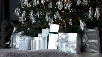 Christmas tree with modern silver decorations and gifts at home. New Year decoration and festive Christmas mood. Christmas tree with stylish decor.