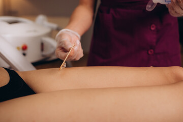 Preparation of clients legs before laser hair removal procedure in spa salon. Beauty master in black gloves applies special gel to the legs of woman with pink pedicure. Copy space.