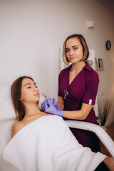 Obraz na płótnie Canvas Professional female beautician makes a rejuvenating injection to a young woman who lies relaxed with her eyes closed in a modern beauty salon. Concept of smoothing wrinkles with injections.