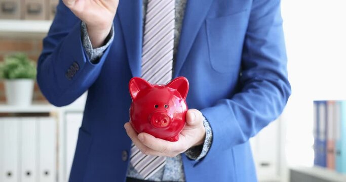 Businessman tosses coins into red piggy bank. Saving savings concept