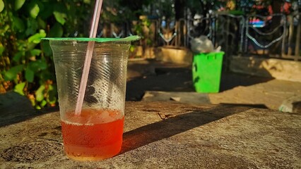 The leftovers of a plastic cup of tea with straw on the table in the city park