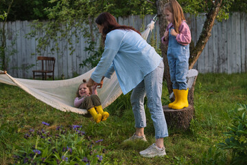 Naklejka na ściany i meble Capturing spontaneous family joy: Two siblings experience hammock fun while their mother ensures safety, surrounded by evening's soft light
