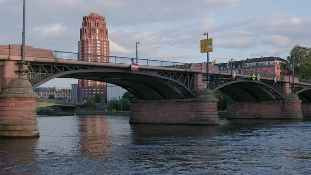 Pan across the Ignatz Bubis Bridge over the River Main in Frankfurt on a summer evening. The Lindner Hotel is seen behind 