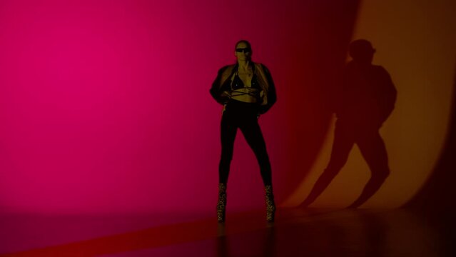 Young woman dancer dancing in leather bra and high heels in the studio, orange and red neon light vibrant background.