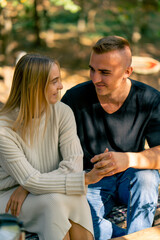 Cute young couple guy and girl smiling and talking while sitting together on sunny day in nature