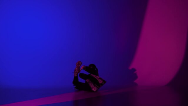 Adult woman dancer dancing in leather bra and high heels in the studio, blue and pink neon light vibrant background.