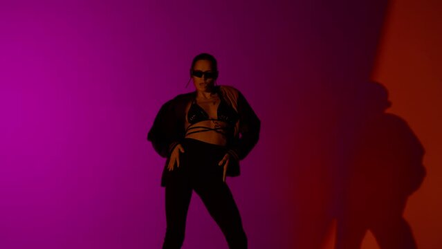 Appealing woman dancer dancing in jacket and on high heels in the studio, red and purple neon light vibrant background.