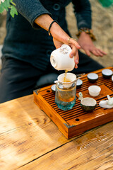 Fototapeta na wymiar The hands of a professional tea master who pours fresh natural green tea from a glass teapot into bowls on wooden chaban table