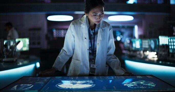 Female Asian Neuroscinetist Using Interactive Touch Screen Table With MRI Scans On Display In Modern Biotechnology Research Center. Doctor Developing Innovative Devices For People With Brain Damage.