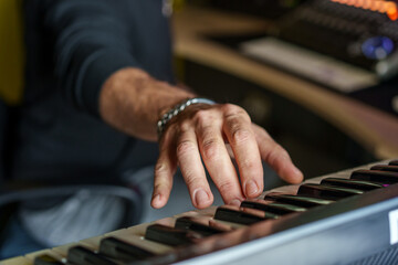 Close-up of a musician's hands playing an electronic keyboard with focus on fingers and keys,...