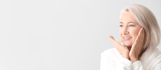 Mature woman giving herself face massage on light background with space for text