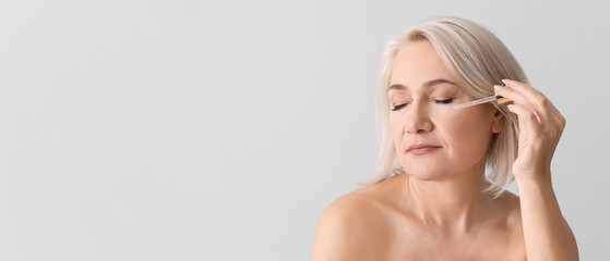 Mature woman applying face serum against light background with space for text