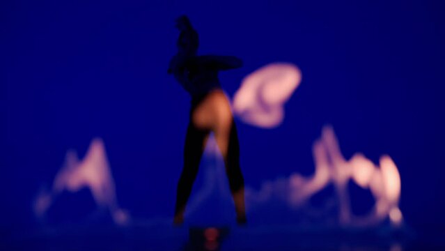 Silhouette of attractive woman dancing modern choreography on high heels in the studio on blue background behind flame.
