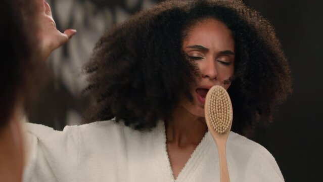 Female reflection in mirror dancing crazy funny singing happy beautiful African American woman sing in bath brush fooling around beauty procedure routine bathroom lady with curly hair girl having fun