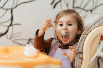 Cute little child girl eating yogurt indoors