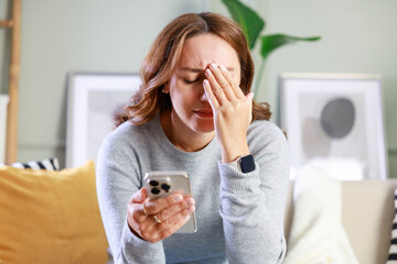 Frustrated young woman with a smartphone in hands while she sitting on the couch at home