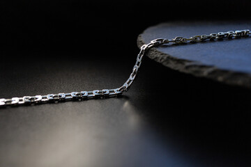 A silver chain lies against a black stone background