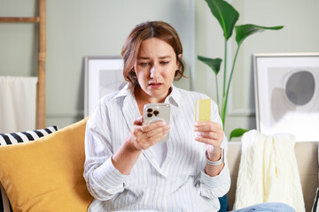 Anxious woman looking at smartphone and having trouble paying credit card