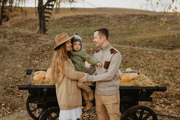 Young mom and dad with their little son hugging and walking on a pumpkin farm. Autumn.