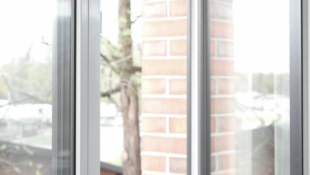 A man's hand turns the handle of the window frame and opens a PVC plastic window, letting in fresh air and changing the temperature and humidity in the room.