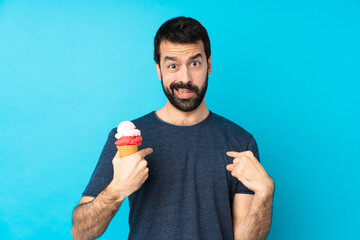 Young man with a cornet ice cream over isolated blue background pointing to oneself