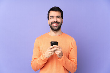 Caucasian handsome man over isolated purple background sending a message with the mobile