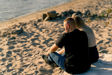 Silhouette of couple in love sitting on the sandy bank of the river admiring the setting sun and...