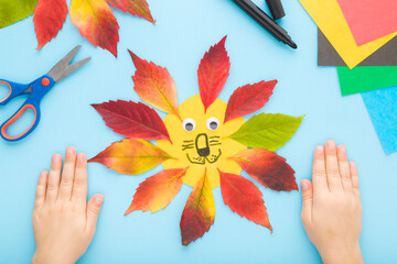 Little child hands creating lion head shape from colorful leaves and paper on light blue table...