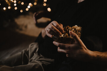 Hands close-up. A guy and a girl are holding a bucket of popcorn on the background of a Christmas...