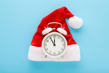 Alarm clock on bright red hat with white fur on light blue table background. Pastel color. Closeup....