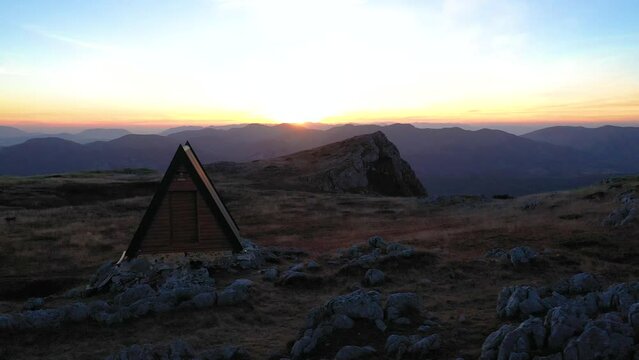 A beautiful small a-frame mountain shelter house with hiker taking photos of a sunset