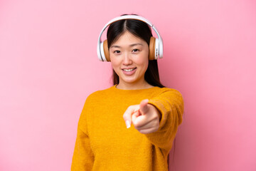 Young Chinese woman isolated on pink background listening music and pointing to the front