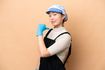 Young Chinese Fishmonger woman wearing an apron and holding a raw fish isolated on pink background proud and self-satisfied
