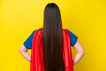 Young Chinese woman isolated on yellow background in superhero costume in back position © luismolinero