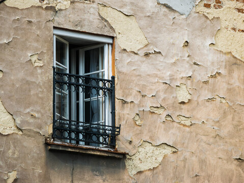 Window with a metal grill on an old wall with peeling plaster