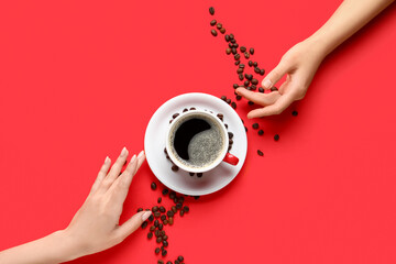 Female hands with cup of hot coffee and beans on red background