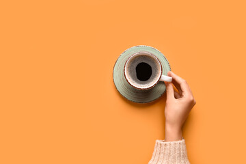 Woman holding cup of hot coffee on orange background