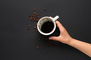 Woman holding cup of hot coffee and beans on black background