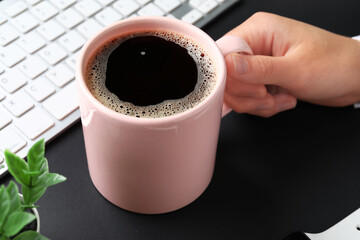 Woman holding cup of hot coffee and keyboard on black background