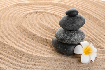 Fototapeta na wymiar Stack of zen stones with white flower on sand. Harmony with nature concept