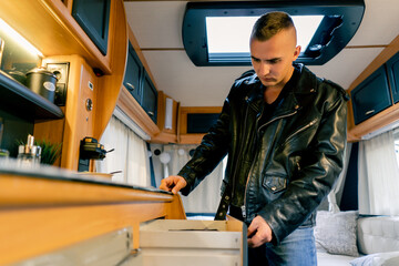 A man opens drawers and cabinets in the kitchen in search of a cup to make tea in motor home