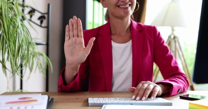 A woman sitting in the office affably waves her hand, a close-up. Meeting and parting at the workplace