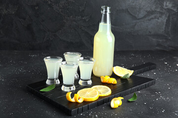 Board with shots and bottle of tasty Limoncello on black background