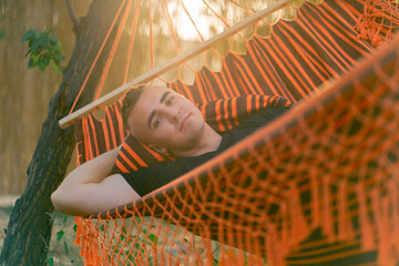 A guy lies relaxed in a hammock resting and relaxing at sunset while vacationing in glamping in countryside