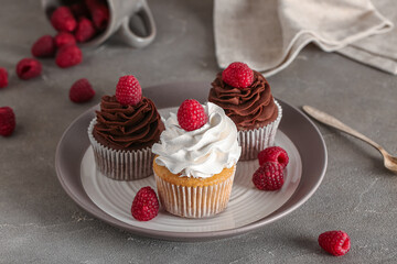 Plate of tasty cupcakes with raspberries on grey background