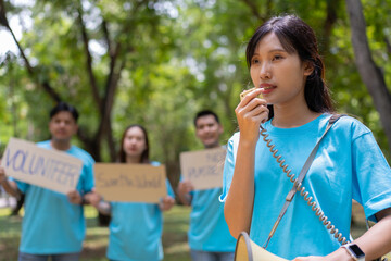 Fototapeta premium Happy young Asian students diverse volunteers hold a campaign sign for cleaning in the park, The concept of environmental conservation on world environment day, recycling, charity for sustainability.