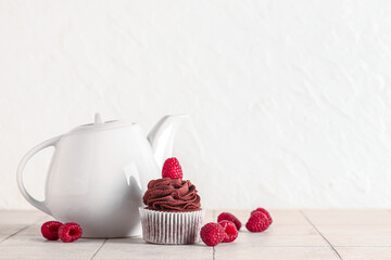Tasty chocolate cupcake with raspberries and teapot on table
