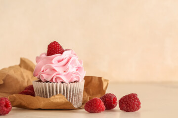 Tasty raspberry cupcake and fresh berries on beige background